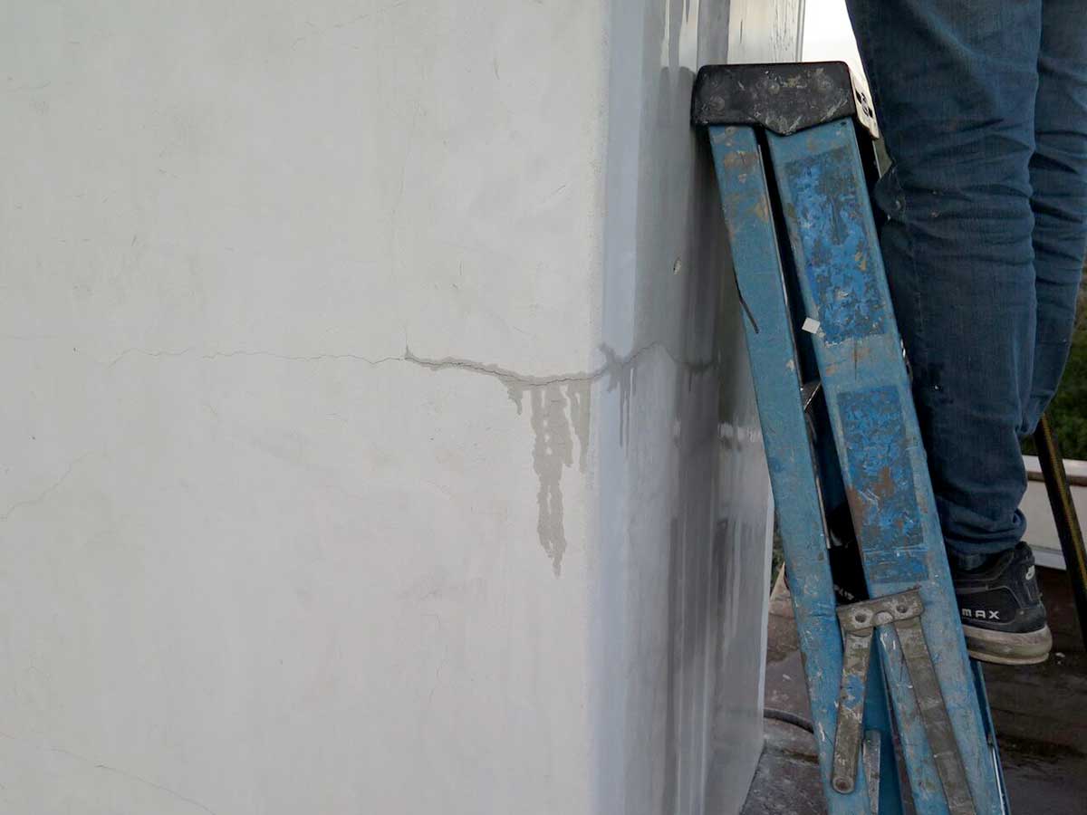 Roof consultants examining wet stucco crack on wall in Austin, Texas.